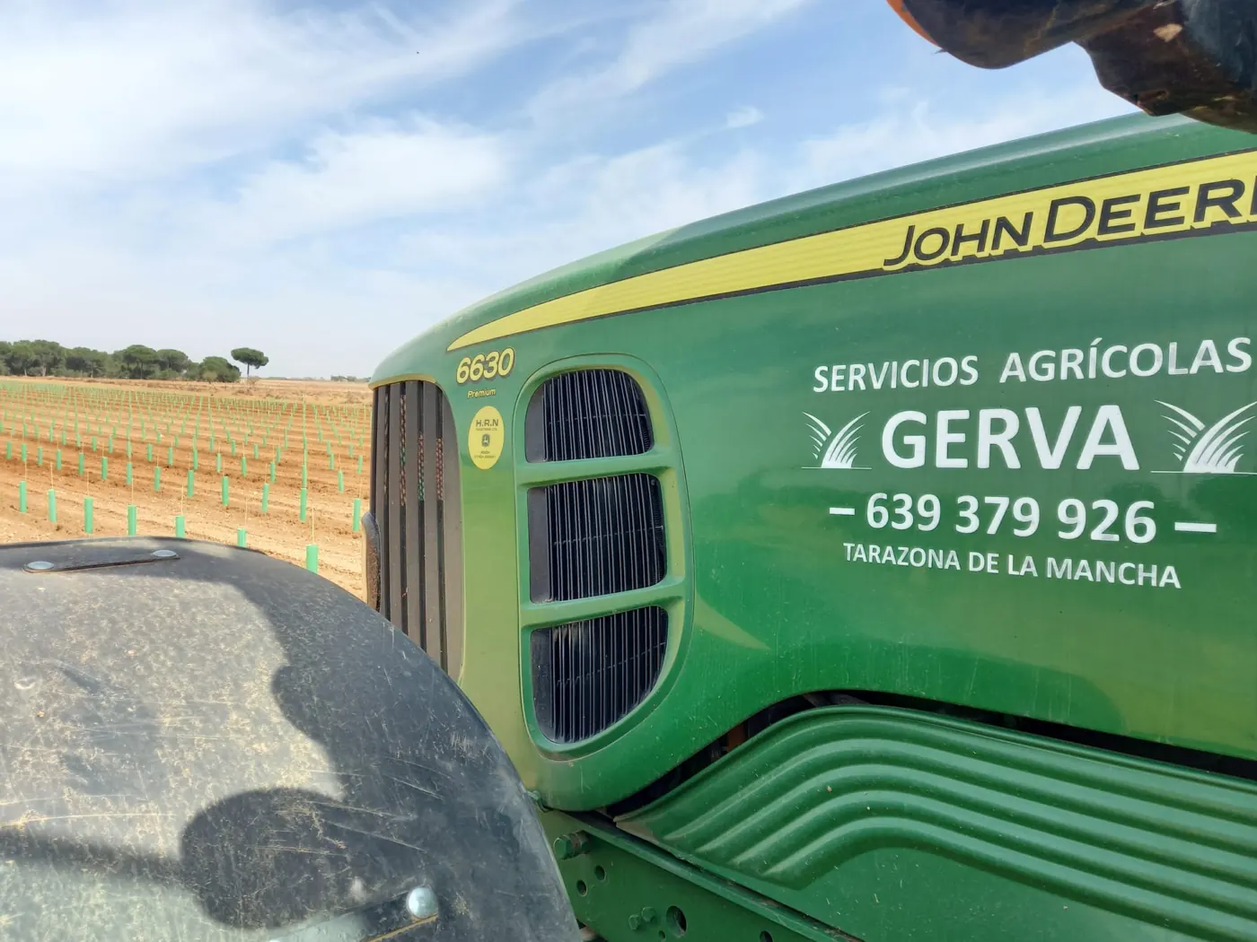 Tractor rotulado con el logo de Servicios Agrícolas Gerva junto a una plantación